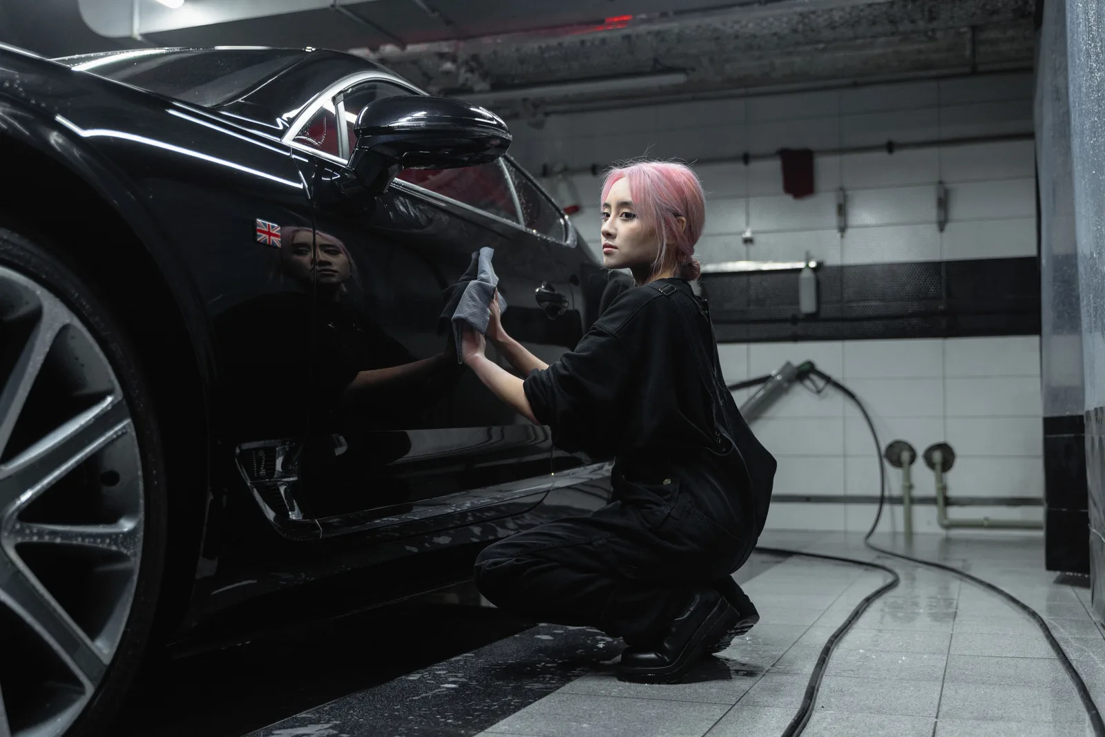 A valeter wiping the side of a black car with a cloth in an indoor wash bay